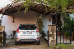 Moderný hliníkový prístrešok pre auto pri rodinnom dome, ktorý chráni zaparkované vozidlo pred dažďom, snehom a slnečným žiarením.